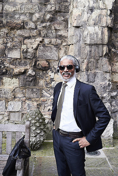 Porträt eines lachenden älteren Geschäftsmannes in Anzug und Krawatte  der mit Kopfhörern Musik hört
