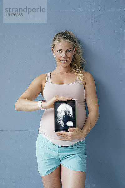 Porträt einer lächelnden schwangeren Frau mit Ultraschallbild auf Tablette