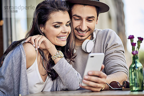 Glückliches junges Paar benutzt Handy im Außencafé