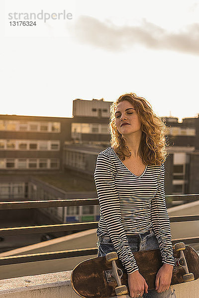Porträt einer jungen Frau mit Skateboard bei Sonnenuntergang auf der Dachterrasse