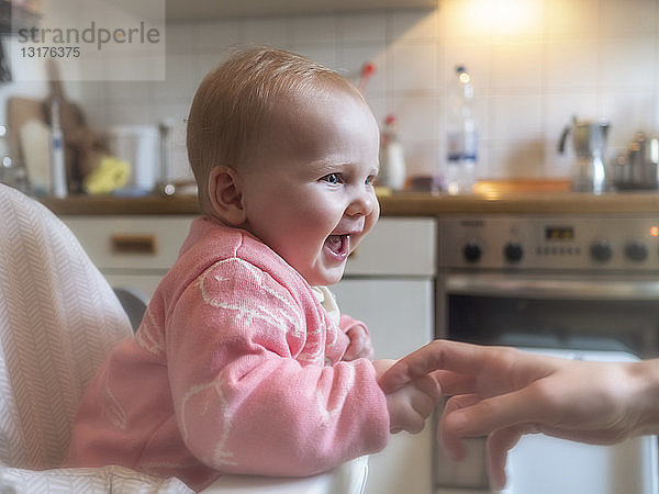 Glückliches kleines Mädchen im Hochstuhl in der Küche sitzend