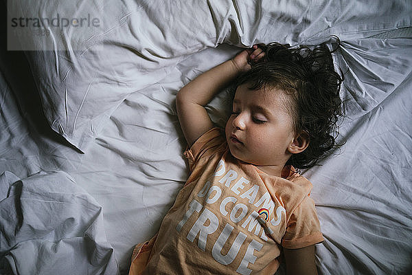 Mädchen schläft im Bett mit T-Shirt-Botschaft 'Träume werden doch wahr'.