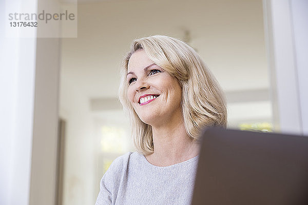 Porträt einer lächelnden blonden Frau mit Laptop zu Hause
