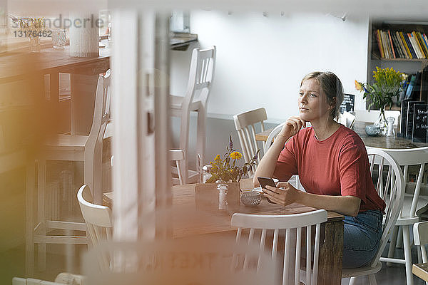 Junge Frau mit Handy sitzt am Tisch in einem Cafe