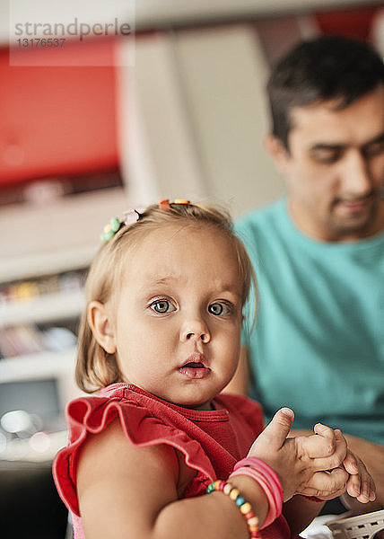 Porträt eines blonden kleinen Mädchens mit ihrem Vater im Hintergrund