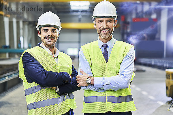 Porträt von zwei lächelnden Managern mit Arbeitsschutzkleidung in der Fabrik