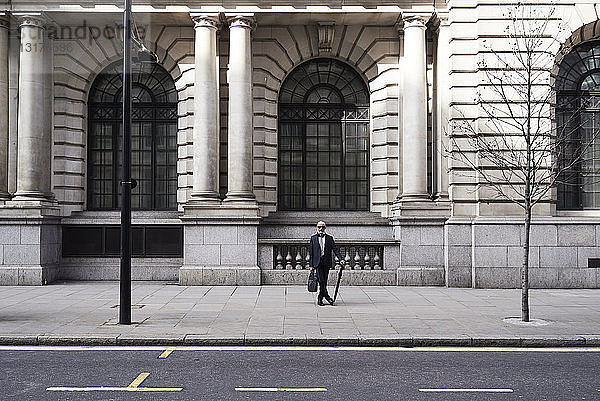 UK  London  stilvoller Senior-Geschäftsmann mit Aktentasche und Regenschirm auf dem Bürgersteig stehend