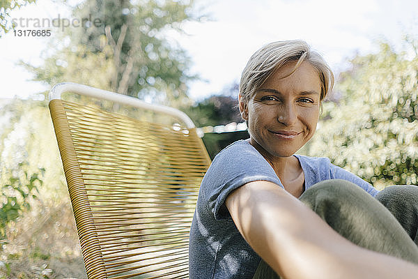 Porträt einer lächelnden Frau  die im Garten auf einem Stuhl sitzt