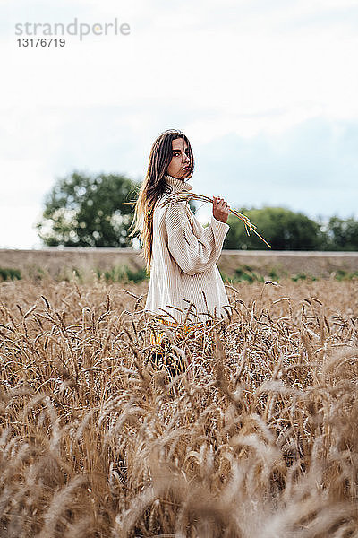 Junge Frau in übergroßem Rollkragenpullover im Maisfeld stehend