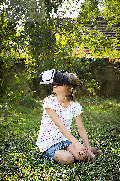 Lächelndes kleines Mädchen mit Virtual-Reality-Brille im Garten