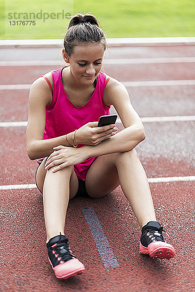Teenagerin sitzt auf der Rennstrecke und benutzt ein Smartphone