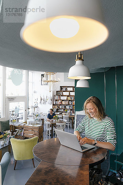 Lächelnde junge Frau mit Laptop in einem Cafe