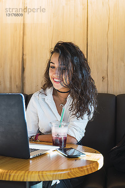 Porträt einer lächelnden jungen Frau in einem Café mit Laptop