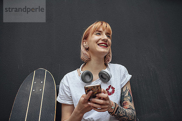 Glückliche junge Frau mit Skateboard  Kopfhörer und Handy