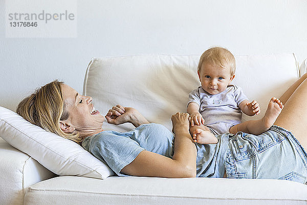 Glückliche Mutter liegt mit ihrem kleinen Mädchen auf der Couch
