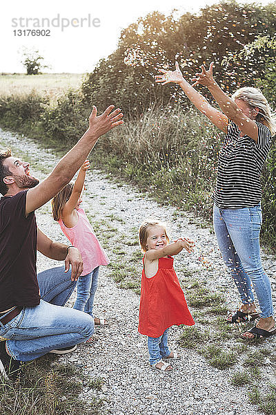 Glückliche Familie mit zwei Töchtern  die auf einem Feldweg mit Konfetti spielen