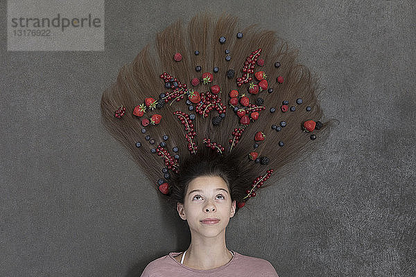 Porträt eines auf dem Boden liegenden Mädchens mit Früchten im Haar