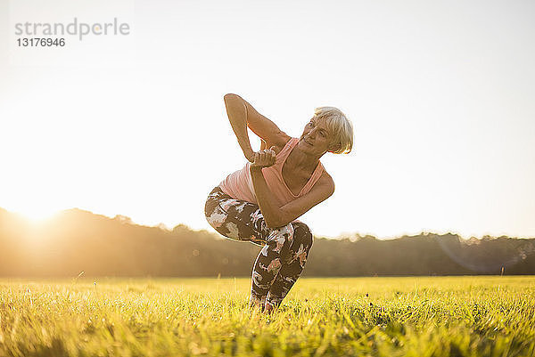 Ältere Frau macht Yoga auf einer ländlichen Wiese bei Sonnenuntergang