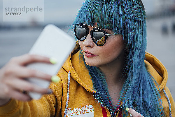 Porträt einer jungen Frau mit gefärbten blauen Haaren  die mit einem Smartphone Selbstgespräche führt
