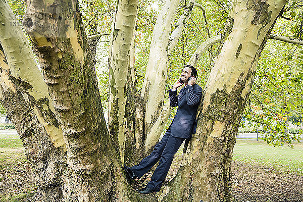 Lächelnder Geschäftsmann mit Kopfhörern an einem Baum