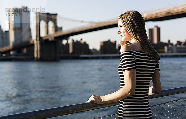 USA  New York  Brooklyn  Frau in gestreiftem Kleid steht bei Sonnenuntergang vor dem East River