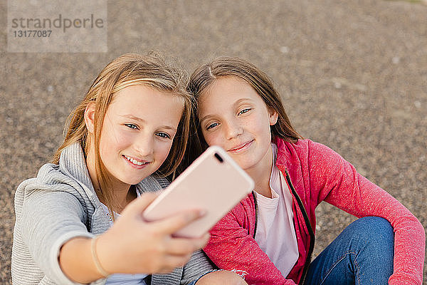 Porträt von zwei lächelnden Mädchen  die sich mit einem Smartphone selbstständig machen