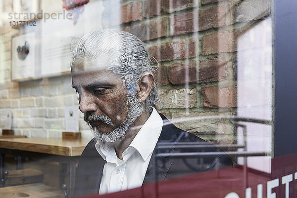 Leitender Geschäftsmann hinter einer Fensterscheibe in einem Café