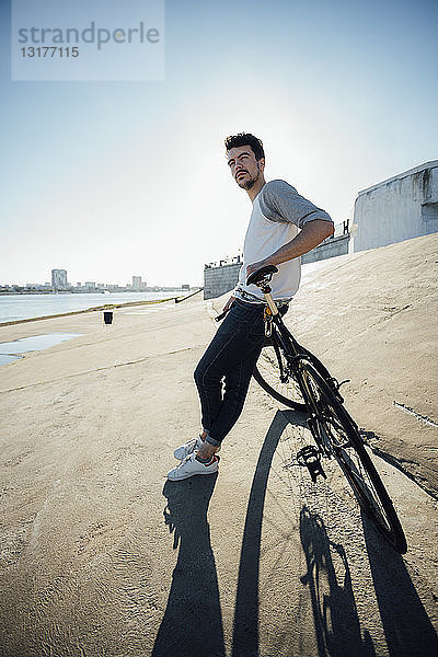 Junger Mann mit Pendler-Fixie-Fahrrad macht Pause an Betonmauer