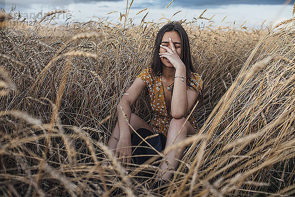 Lachende junge Frau mit Hand auf dem Gesicht im Maisfeld sitzend