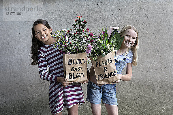 Porträt von zwei lächelnden Mädchen  die Papiertüten mit Blumen halten