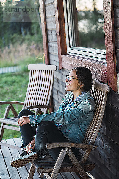 Glückliche junge Frau sitzt auf der Veranda eines Holzhauses