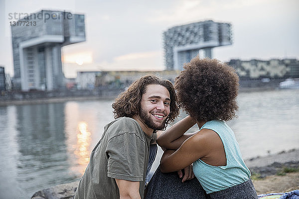 Deutschland  Köln  glückliches Paar entspannt sich bei Sonnenuntergang am Flussufer