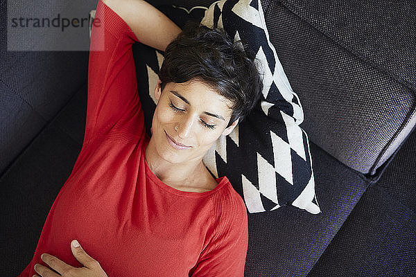 Lächelnde Frau liegt zu Hause mit geschlossenen Augen auf der Couch