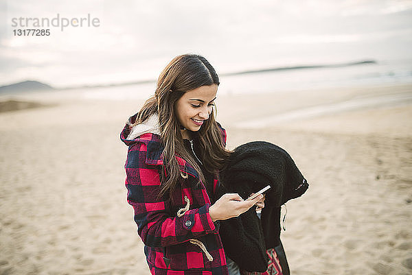 Lächelnde junge Frau mit Smartphone am Strand