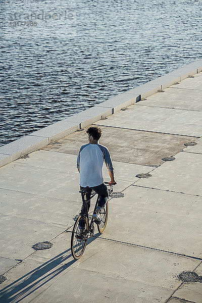 Junger Mann fährt Fahrrad auf der Uferpromenade am Flussufer