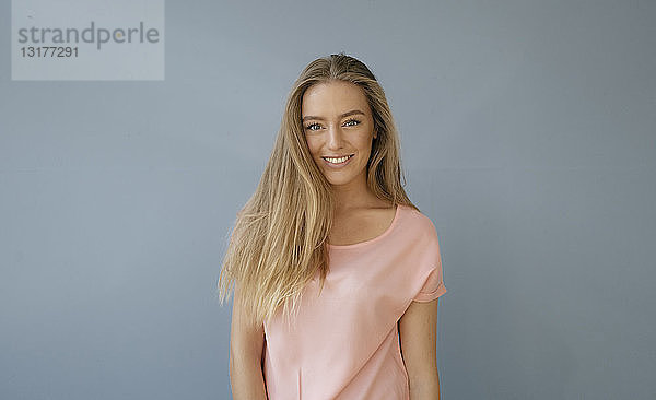 Porträt einer lächelnden jungen Frau mit rosa T-Shirt vor grauem Hintergrund