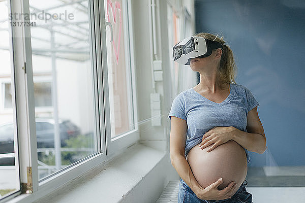Schwangere Frau mit VR-Brille am Fenster