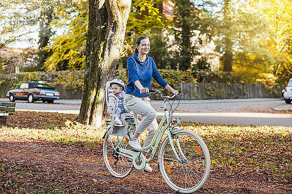 Mutter und Tochter fahren Fahrrad  das Baby trägt einen Helm und sitzt im Kindersitz