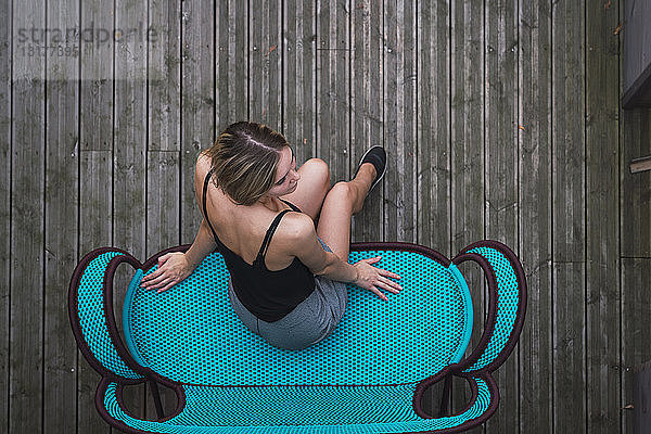 Junge Frau sitzt auf türkisfarbener Couch auf der Terrasse  Draufsicht