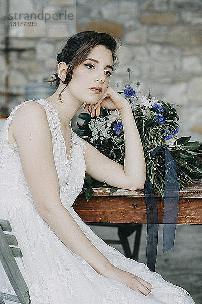 Nachdenkliche junge Frau im Brautkleid am Tisch sitzend