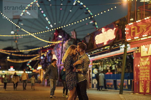 Glückliches junges Paar umarmt und küsst sich auf einer Kirmes