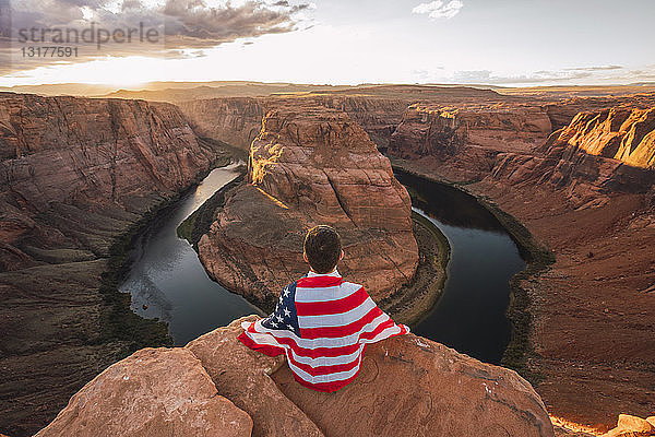 USA  Arizona  Colorado River  Horseshoe Bend  auf Aussichtspunkt sitzender junger Mann mit amerikanischer Flagge