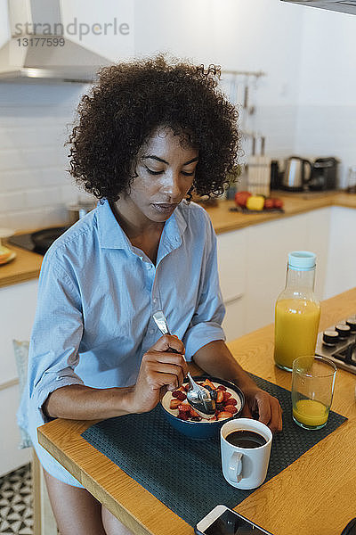 Frau frühstückt in ihrer Küche und isst Obst