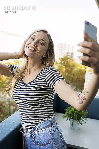 Lächelnde junge Frau mit einem Selfie auf dem Balkon