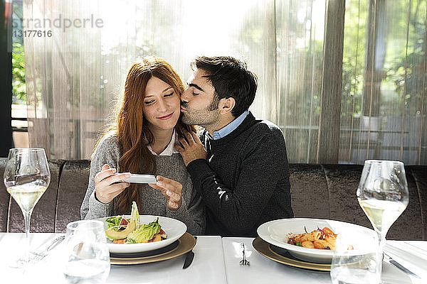 Mann küsst Frau und macht ein Handyfoto in einem Restaurant