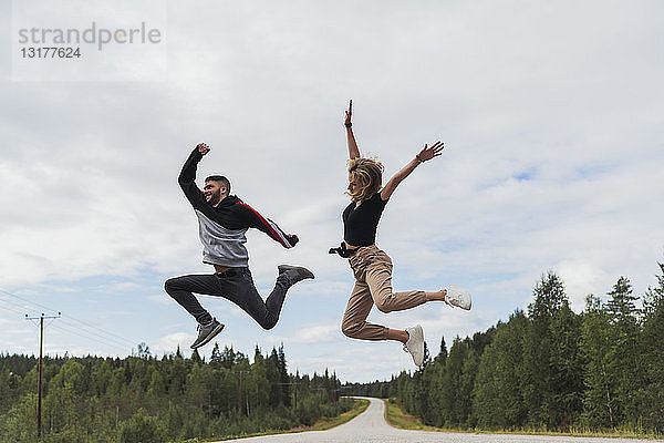 Finnland  Lappland  ausgelassenes junges Paar springt in ländlicher Landschaft
