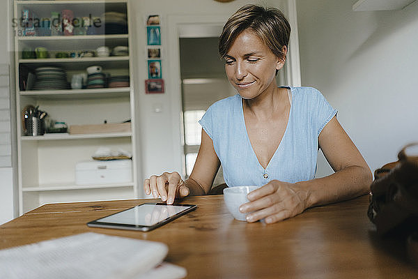 Frau sitzt zu Hause am Tisch mit Tasse Kaffee und Tablette