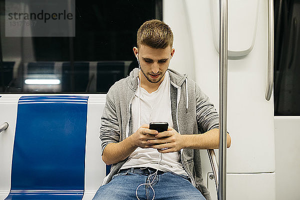 Junger Mann benutzt Smartphone in der U-Bahn