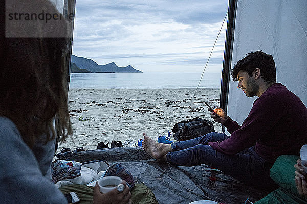 Norwegen  Lappland  Jugendliche zelten in einem Zelt am Strand am Fjord