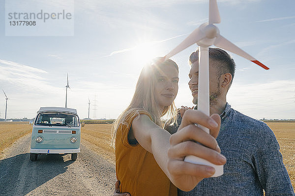 Junges Paar im Wohnmobil in ländlicher Landschaft mit Modell einer Windkraftanlage